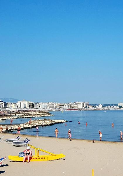 Spiaggia affollata con bagnanti e edifici sullo sfondo.