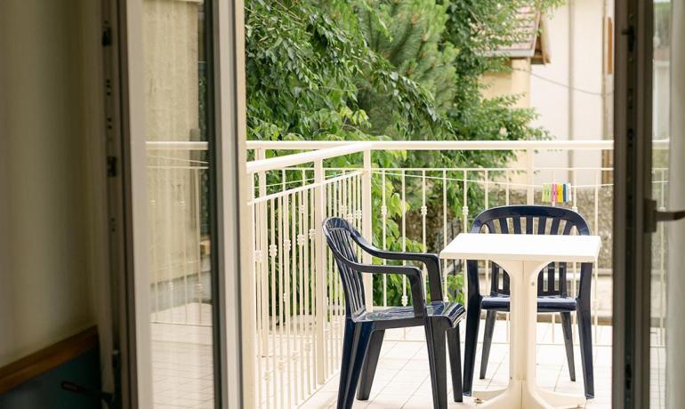 Balcony with chairs and table, overlooking trees.