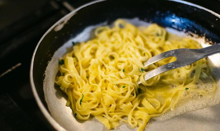 Tagliatelles au beurre dans une poêle avec une fourchette.