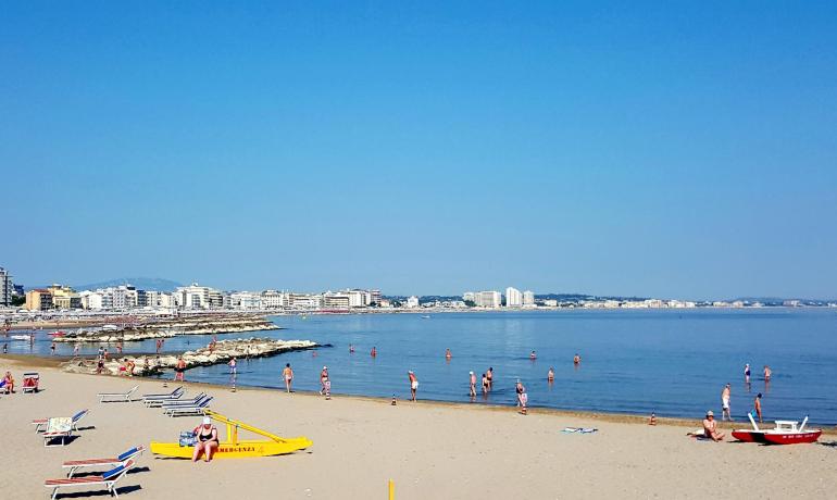 Crowded beach with swimmers and buildings in the background.